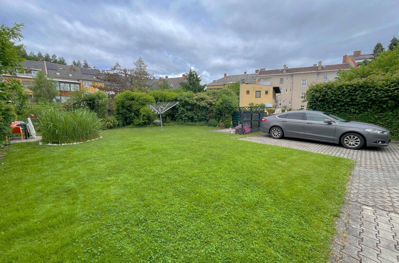 Gepflegter Gartenbereich mit Rasenfläche und einer Wäschespinne, angrenzend an die Einfahrt.