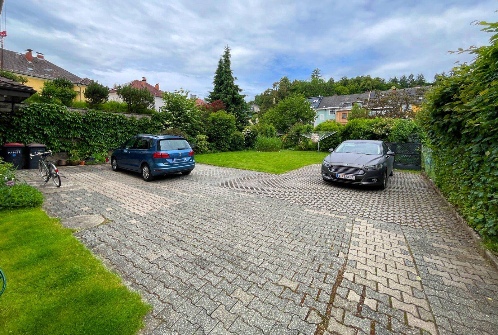 Gepflasterte Einfahrt mit Parkplätzen für zwei Fahrzeuge und grüner Hecke.