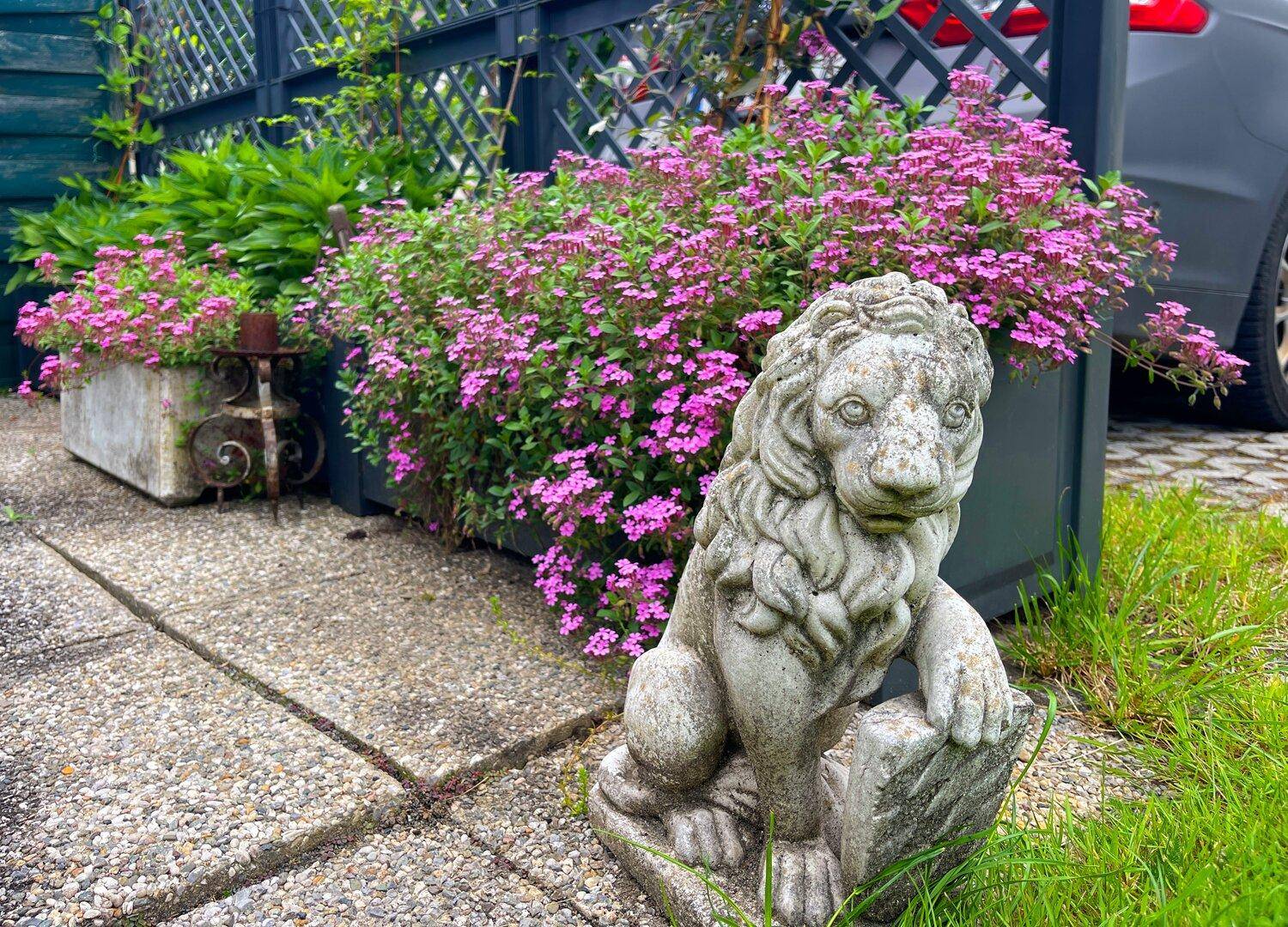 Detailaufnahme einer dekorativen Löwenstatue im Garten, umgeben von blühenden Pflanzen.