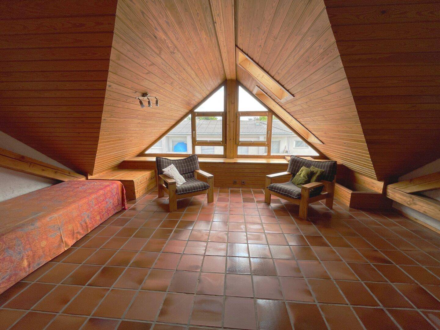 Geräumiger Dachbodenraum mit Holztäfelung, Terrakottafliesen und großen dreieckigen Fenstern.
