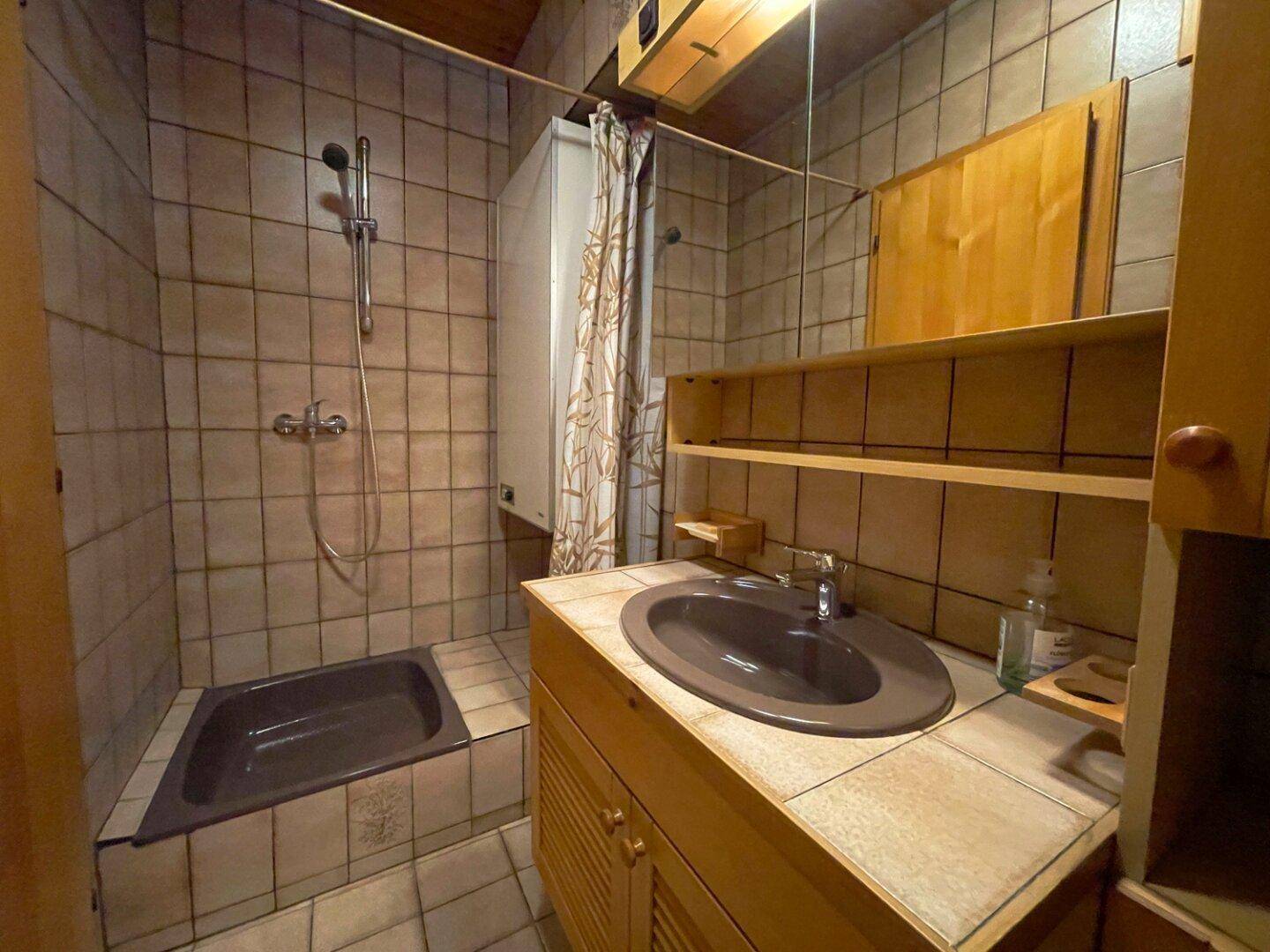 Kleines Badezimmer mit beigefarbenen Fliesen, Duschwanne und Holzwaschtischunterschrank.