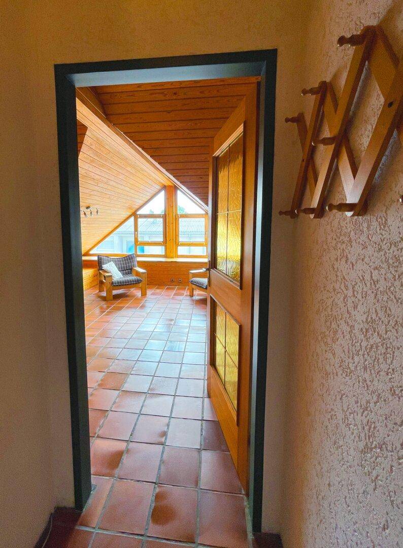 Heller Flur mit Terrakottafliesen und einer Holztür, die in den Dachbodenbereich führt.