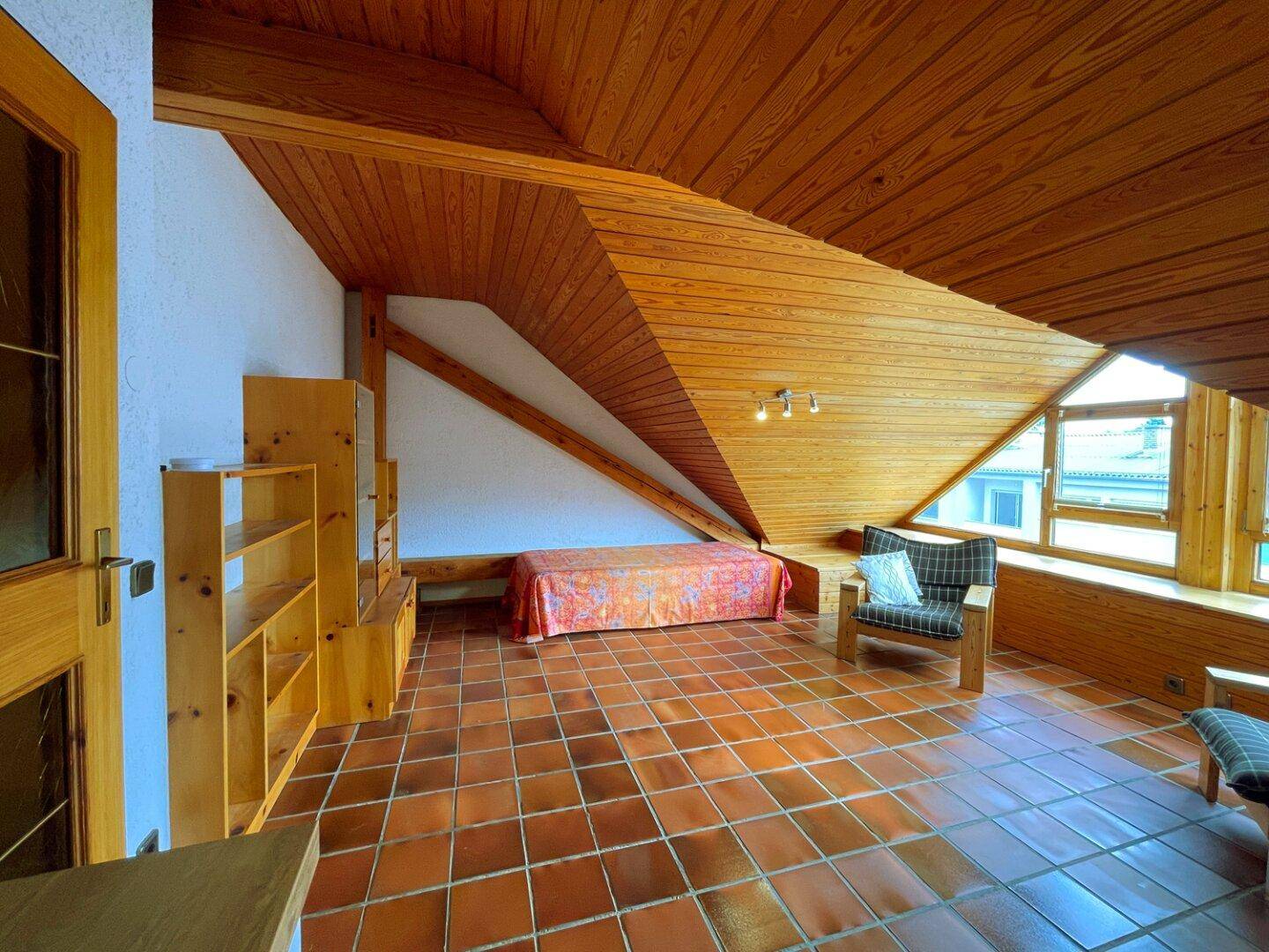 Heller Dachbodenraum mit Holztäfelung, Terrakottafliesen und integrierten Regalen.
