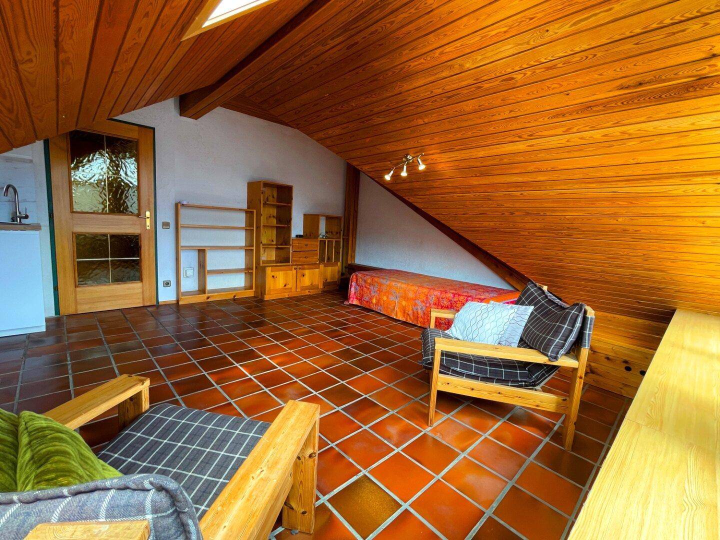 Offener Dachbodenbereich mit Holztäfelung, Terrakottafliesen und einer kleinen Küchenzeile.