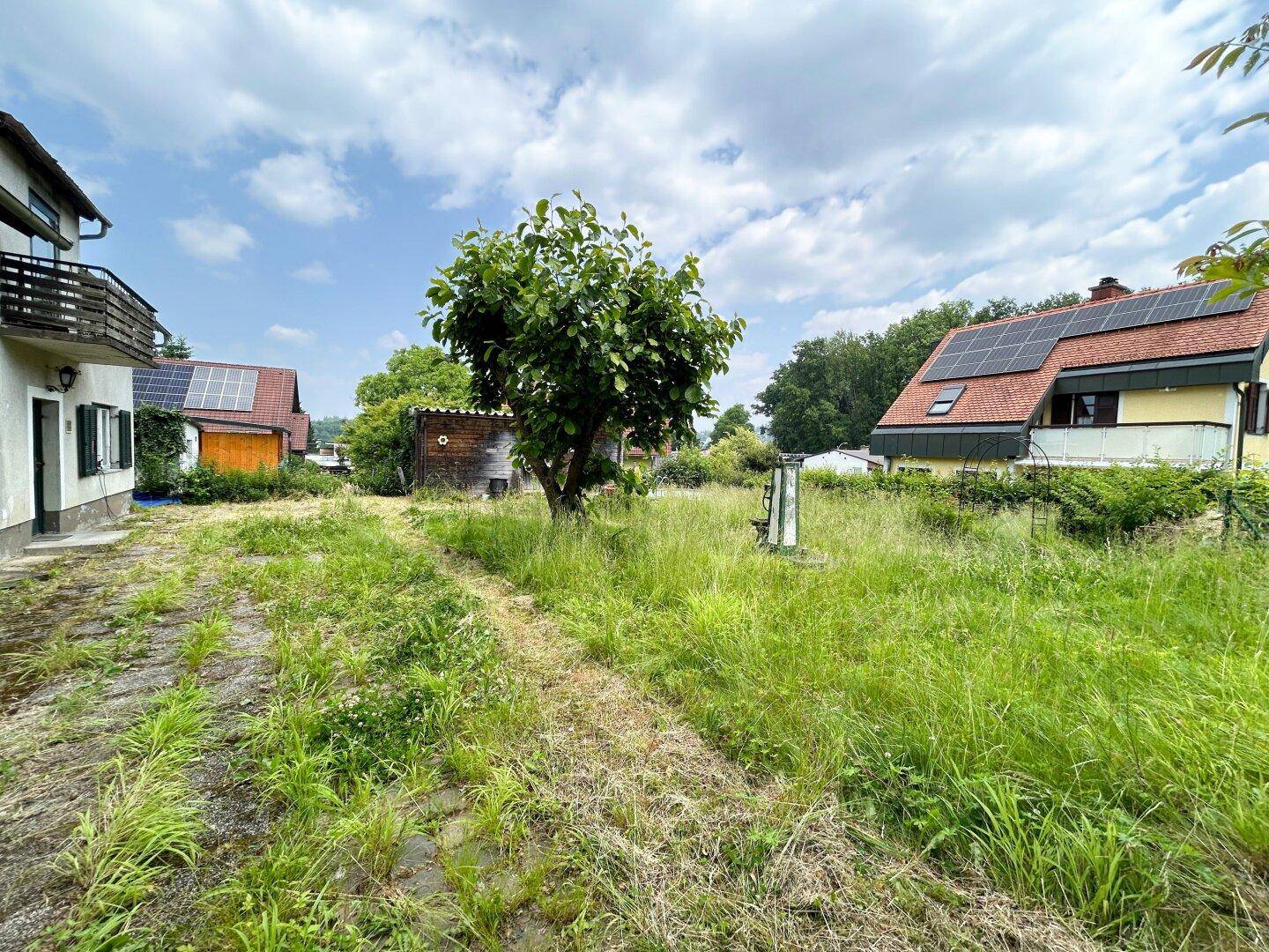 Weitläufiger Gartenbereich mit Blick auf benachbarte Häuser und viel Grün unter blauem Himmel.