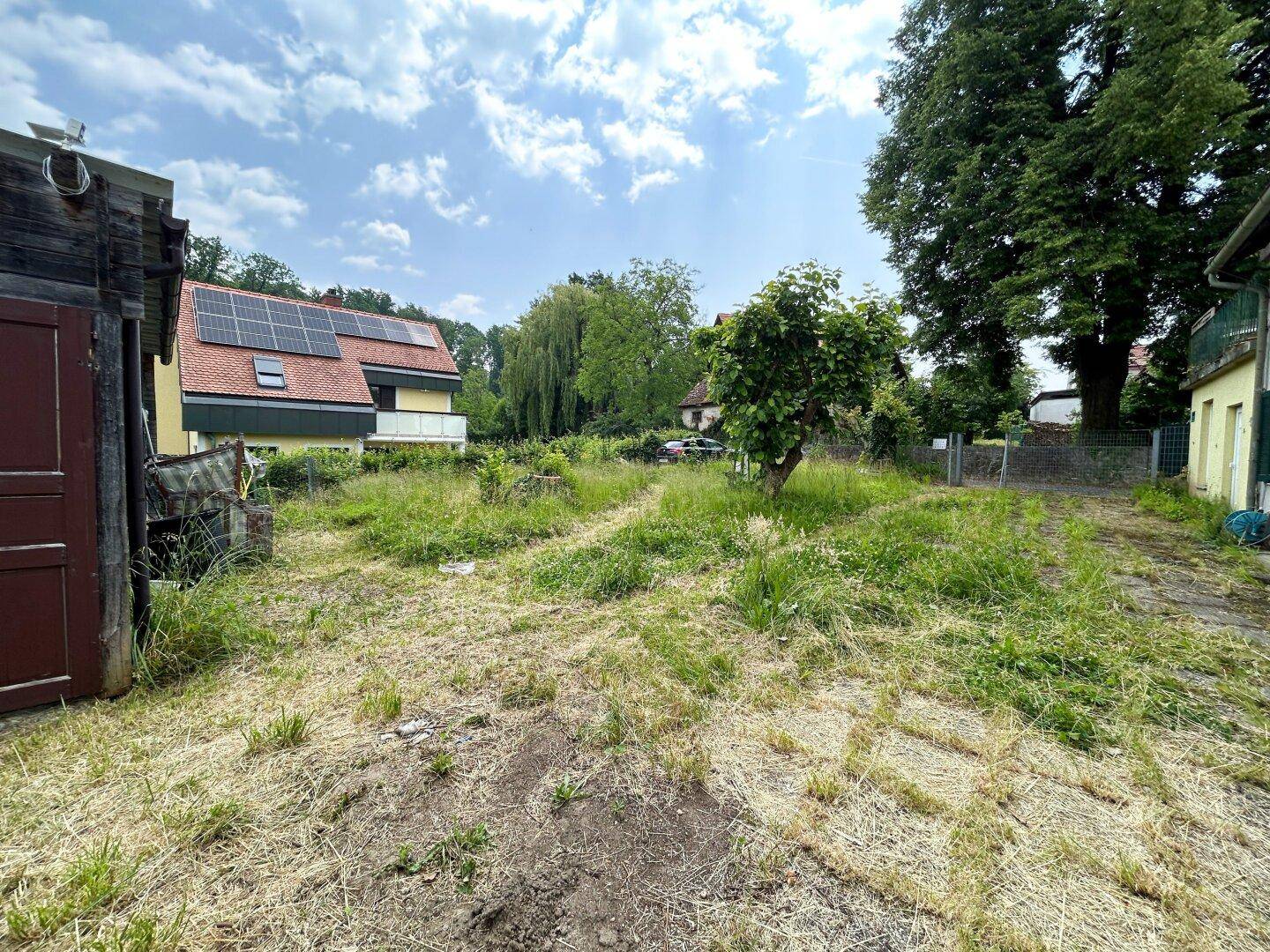 Großer Gartenbereich mit Blick auf die Umgebung und ein Nebengebäude unter blauem Himmel.