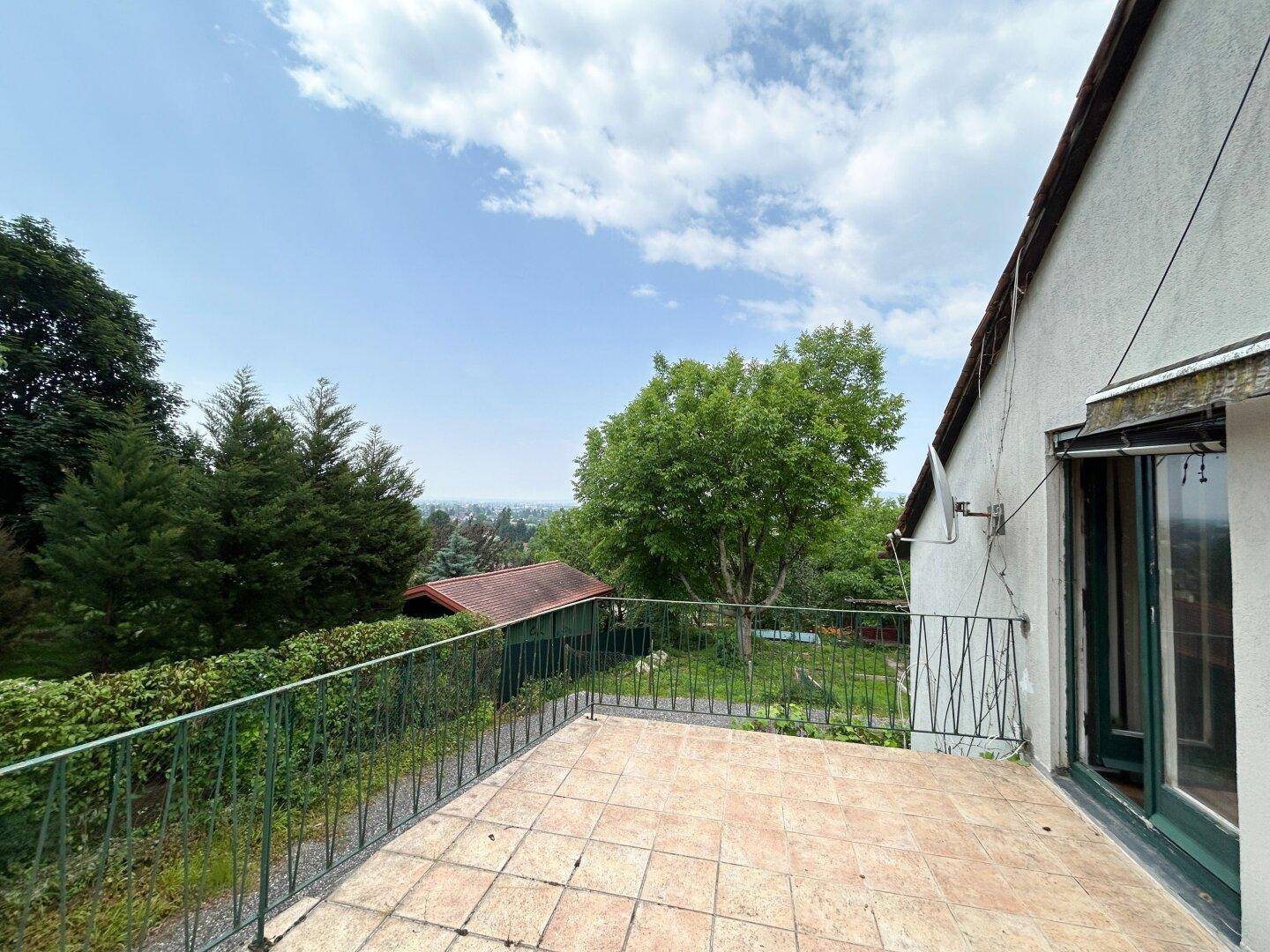 Großer Balkon mit Fliesenboden und weitem Blick über die grüne Landschaft und die Stadt.