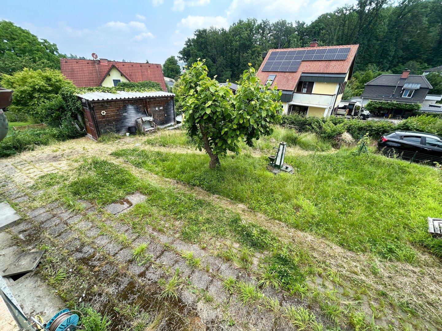 Blick von oben auf den großen, verwilderten Gartenbereich mit benachbarten Häusern.