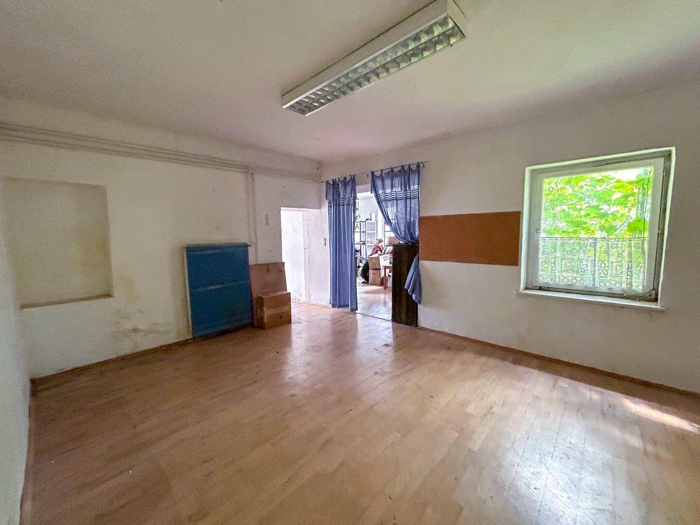 Leerer Raum mit Holzboden, einem Fenster und einer blauen Gardine, die den Eingang verdeckt.