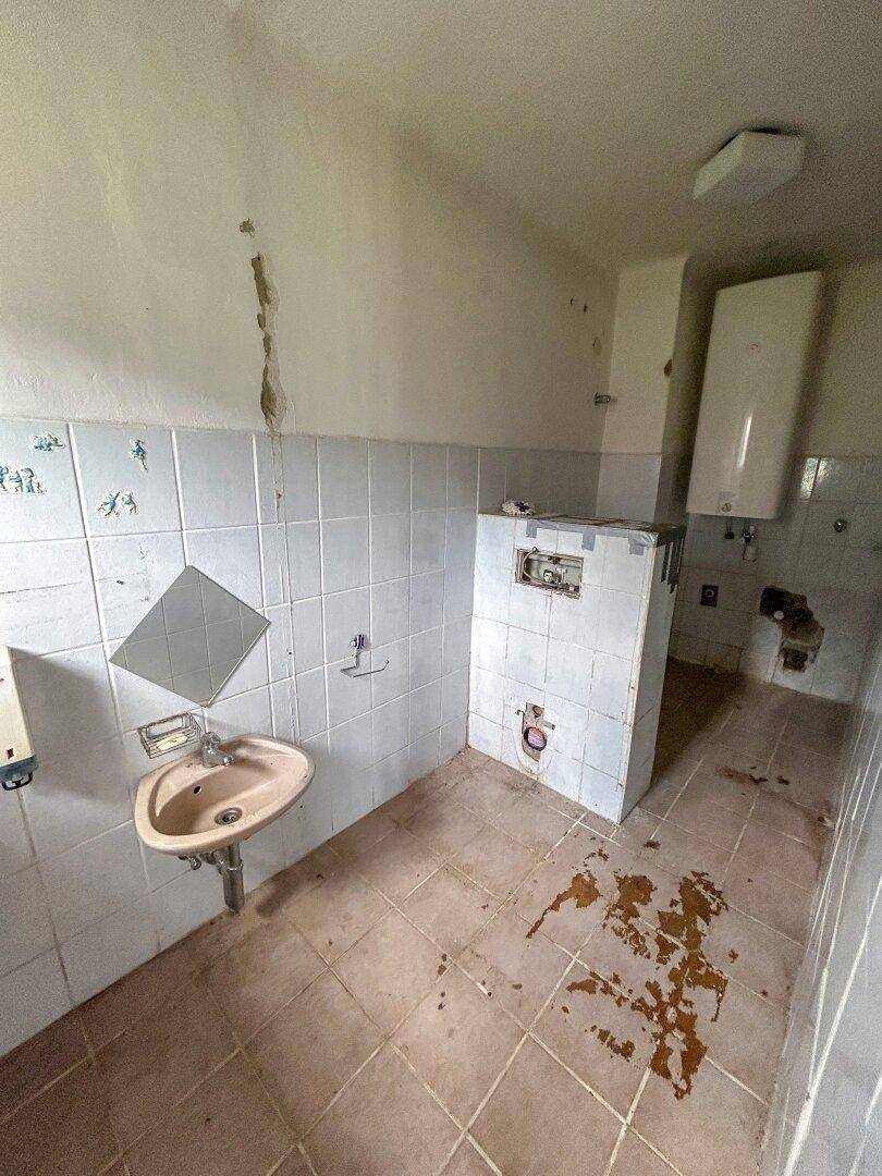 Badezimmer mit Waschbecken, Fliesenboden und einem Warmwasserbereiter an der Wand.