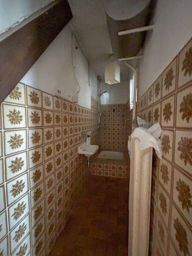 Enges Badezimmer mit Duschbereich, Waschbecken und gemusterten Fliesen an den Wänden.
