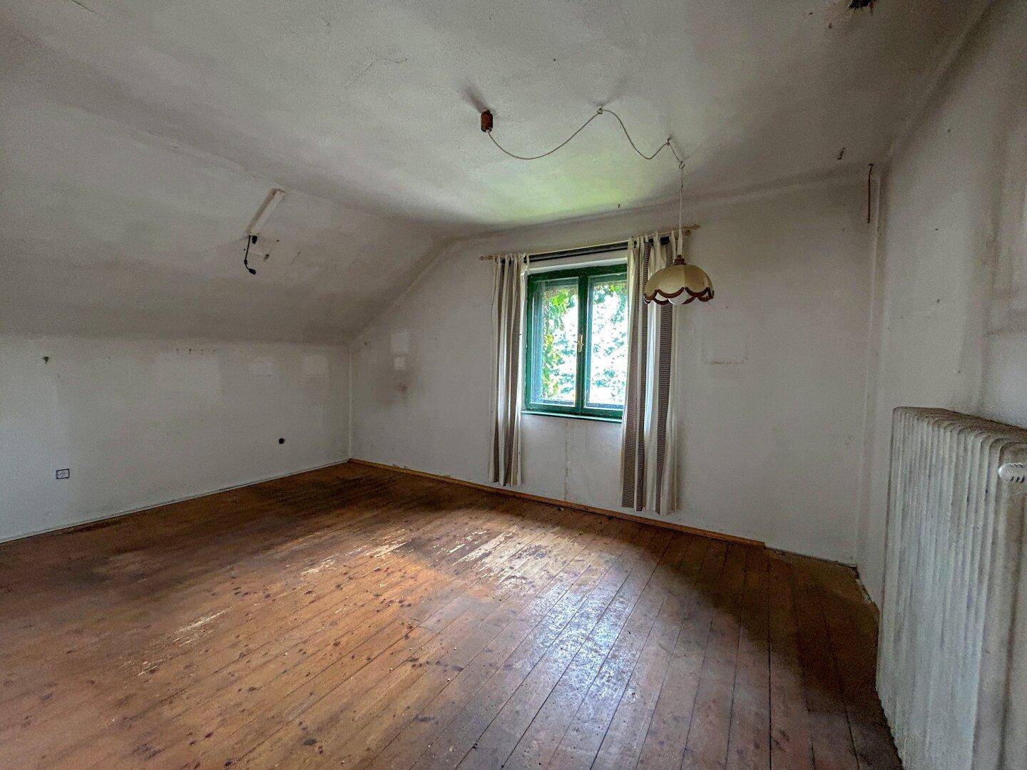 Geräumiges Schlafzimmer im Dachgeschoss mit Holzboden, Fenster und schrägen Wänden.
