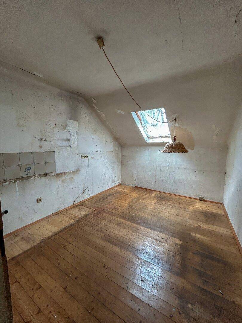 Dachgeschossraum mit Holzboden, Dachfenster und sichtbaren Spuren früherer Nutzung.