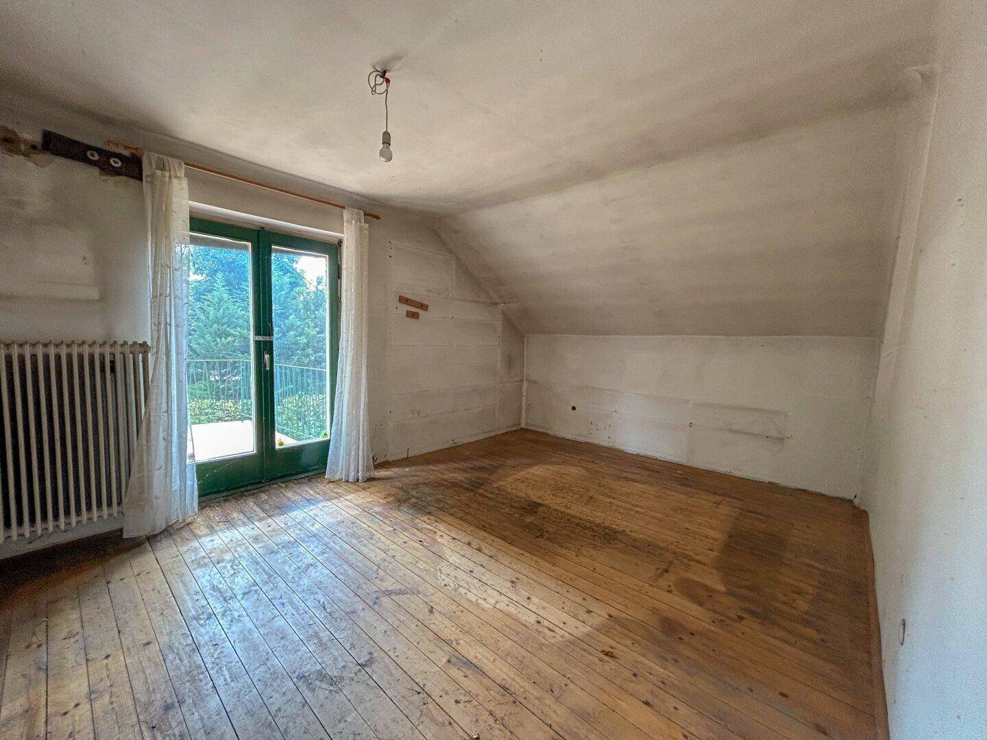 Helles Schlafzimmer im Dachgeschoss mit Holzboden und Zugang zu einem Balkon oder einer Terrasse.