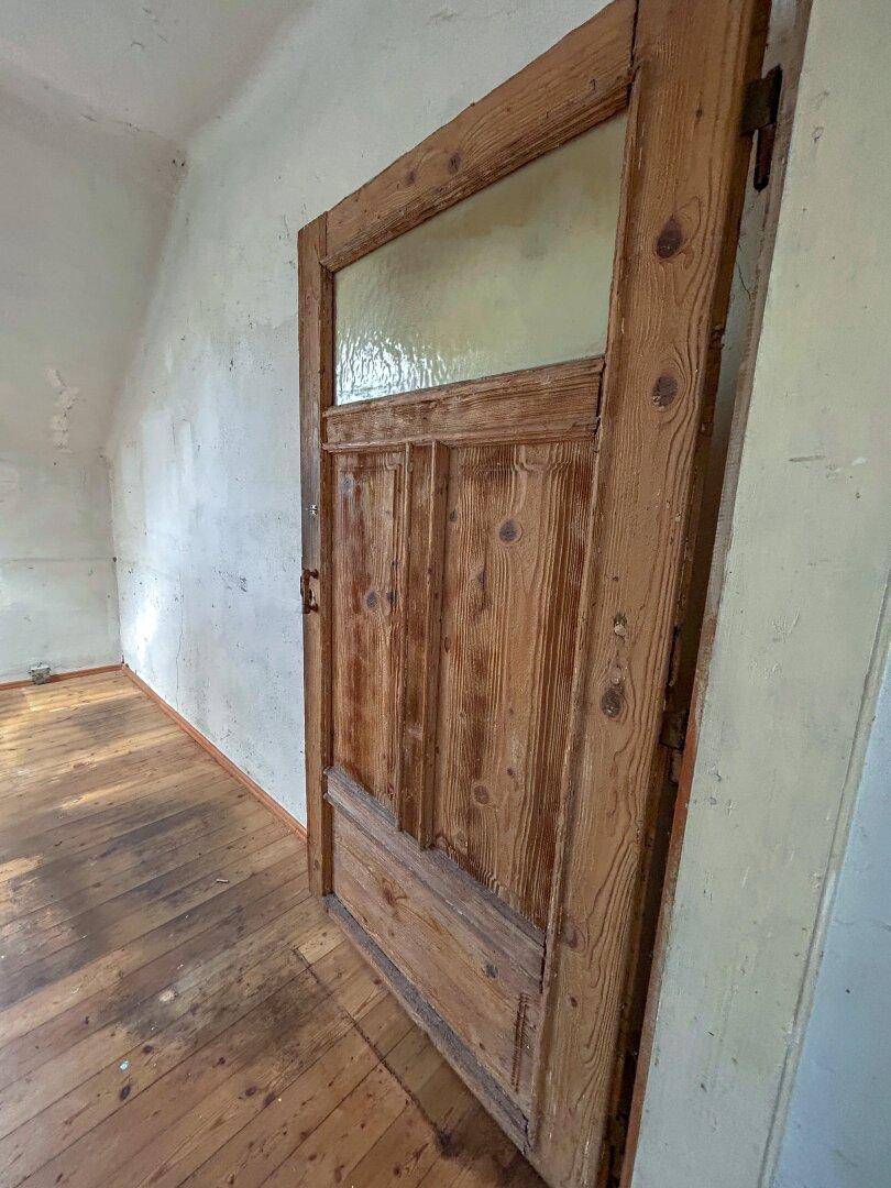 Detailaufnahme einer alten Holztür mit Glaseinsatz und sichtbarer Holzmaserung.