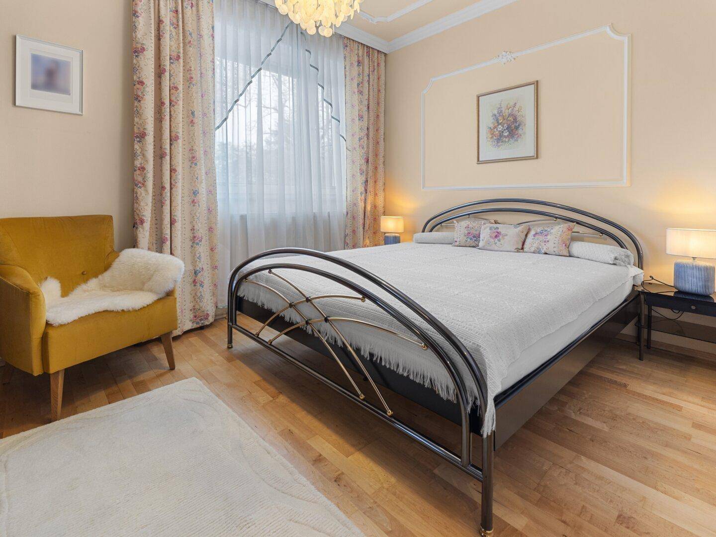 Helles Schlafzimmer mit Doppelbett, Parkettboden und floralen Vorhängen, einladend gestaltet.