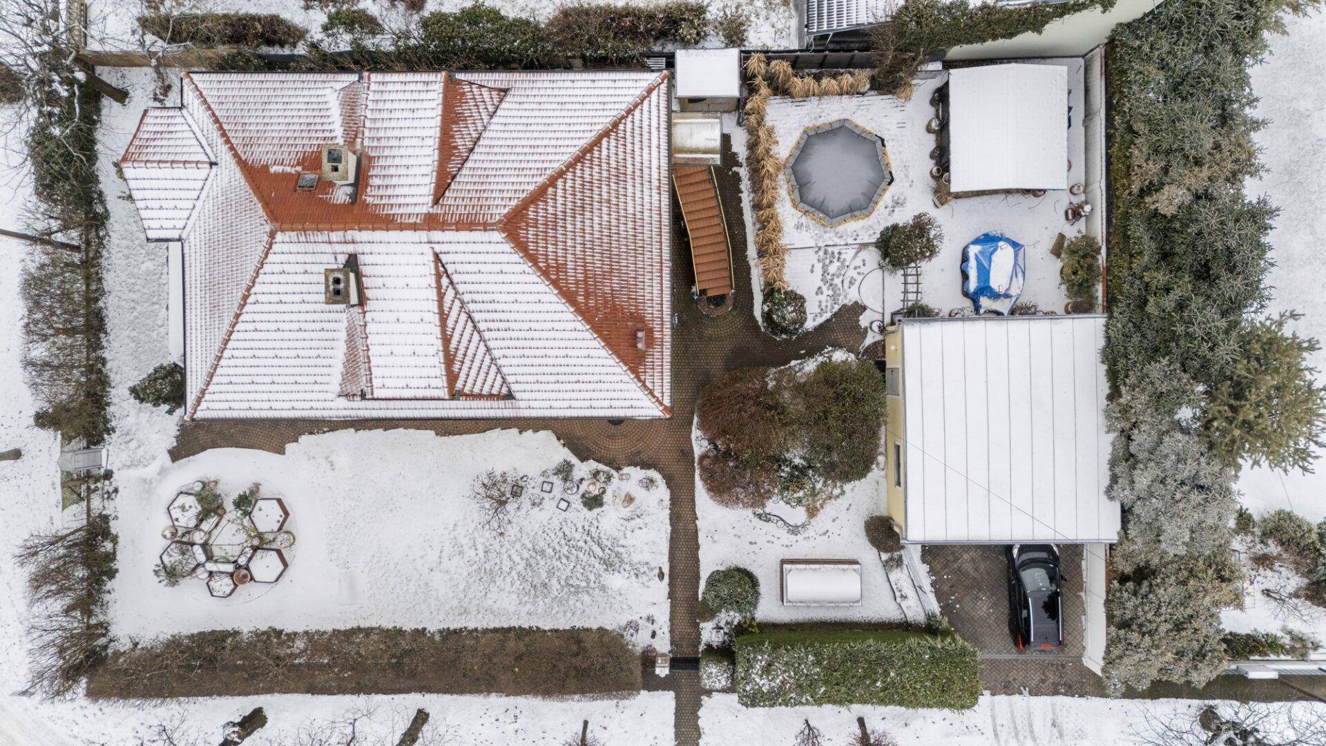Luftaufnahme des Anwesens im Winter mit verschneitem Dach und Gartenbereichen, inklusive Carport.