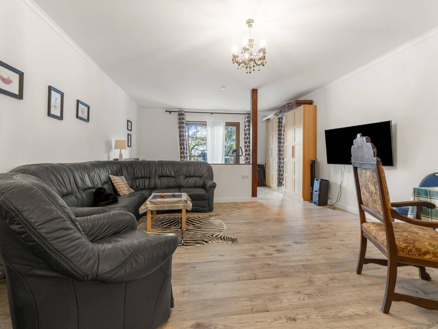 Geräumiges Wohnzimmer mit Ledersofa, Holzboden und Zugang zu einem Außenbereich.