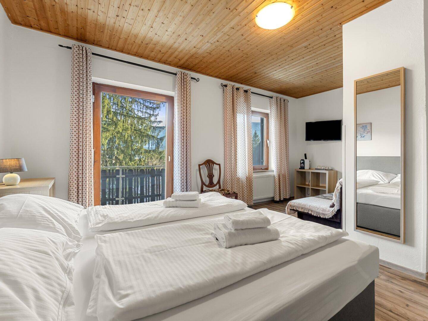 Gemütliches Schlafzimmer mit Holzbalkendecke, Doppelbett und Zugang zum Balkon.