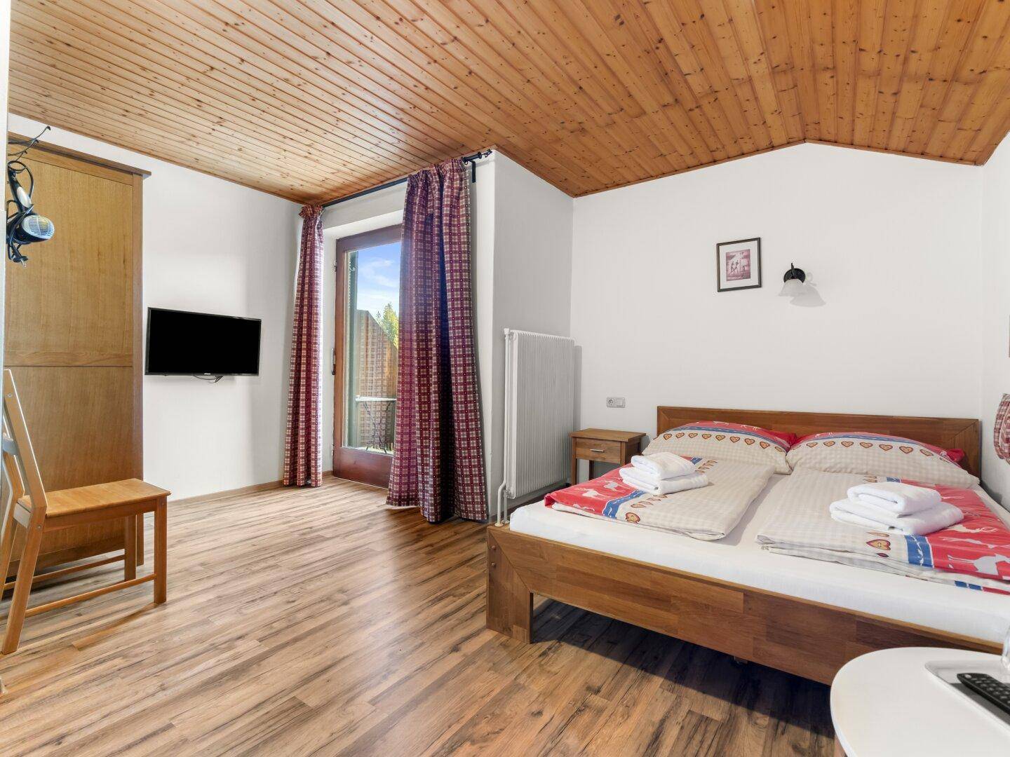 Schlafzimmer mit Holzboden, Holzbalkendecke und Zugang zu einem Balkon.