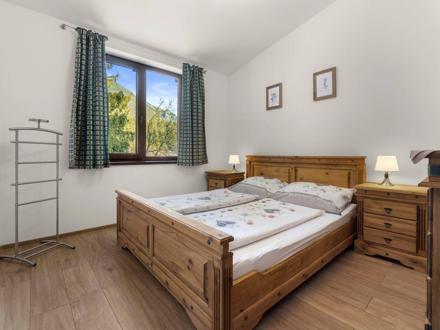 Helles Schlafzimmer mit Holzbett, Nachttischen und Blick auf die grüne Landschaft.