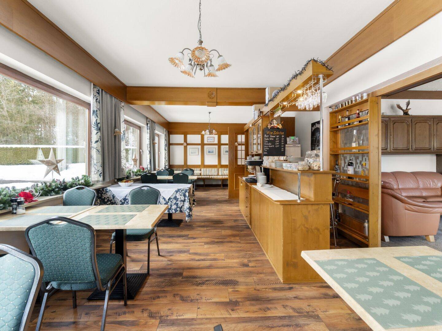 Geräumiger Speisesaal mit Holzbalken, großen Fenstern und Tischen für Gäste.