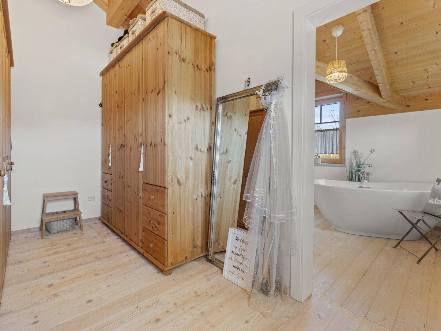 Heller Ankleidebereich mit großem Holzschrank und Zugang zu einem modernen Badezimmer.