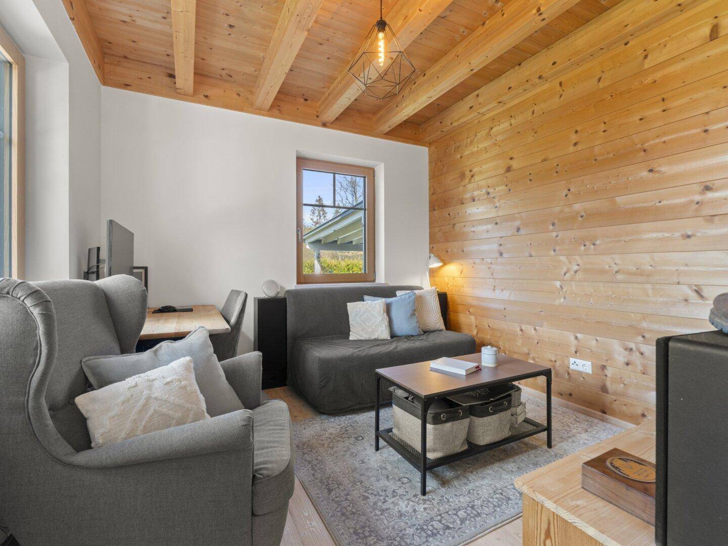 Gemütliches Arbeitszimmer mit Holzwand, Schlafsofa und Blick ins Grüne.