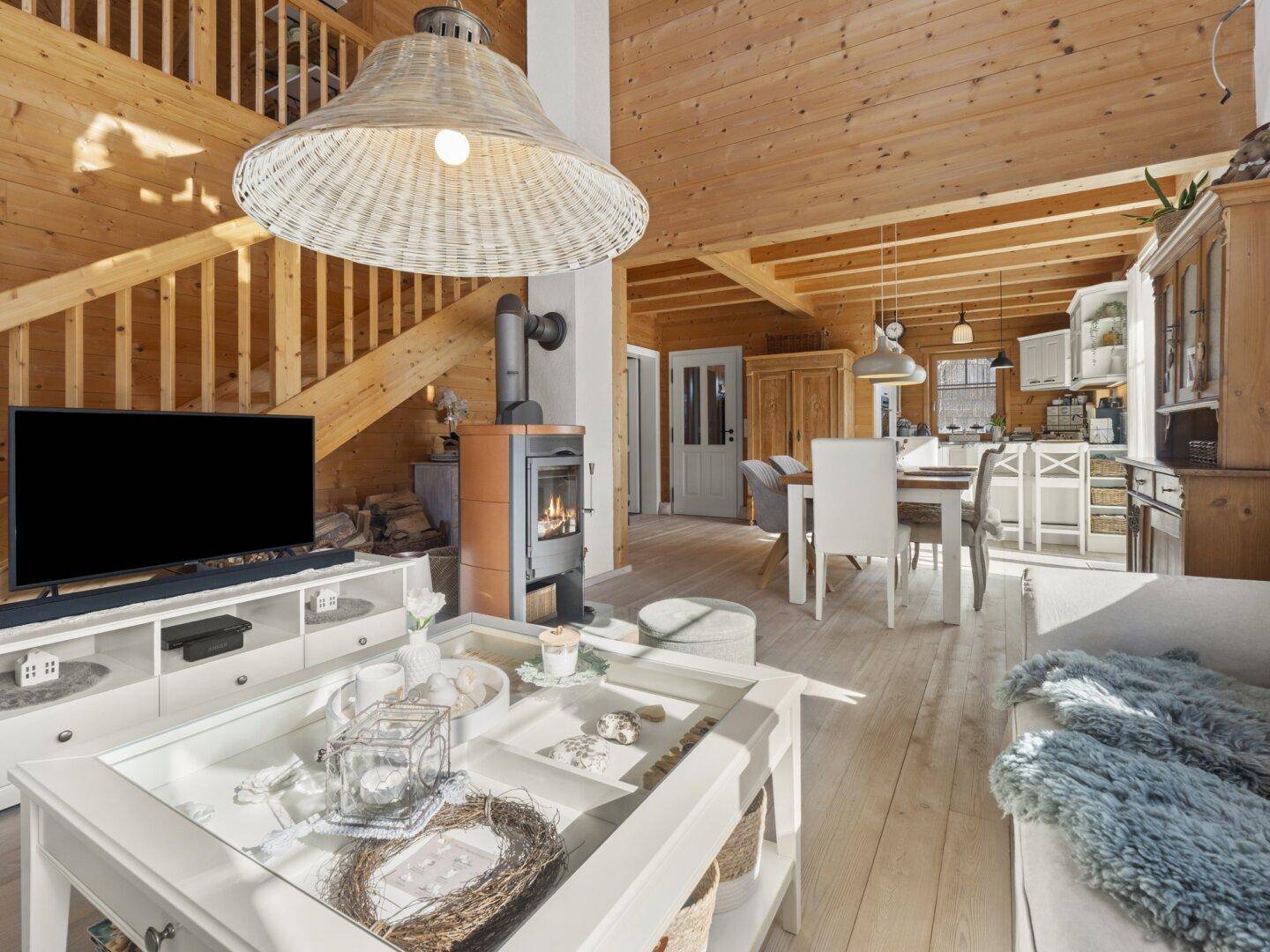 Gemütliches Wohnzimmer mit Holzbalkendecke, Kaminofen und Blick auf den Essbereich und die Küche.