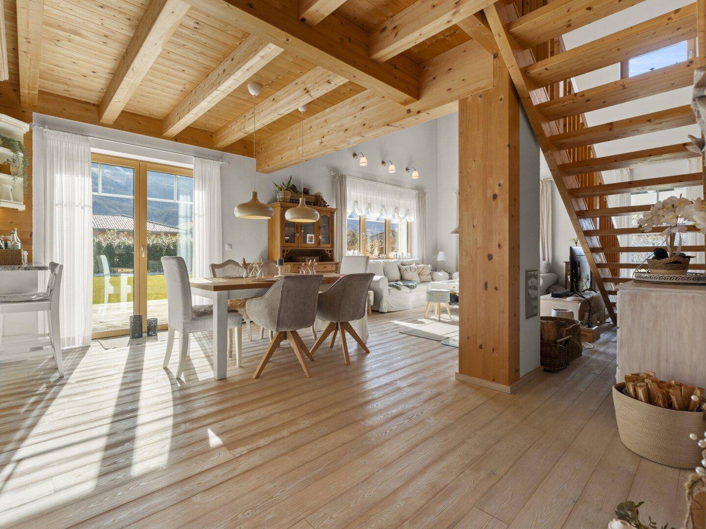 Offener Wohn- und Essbereich mit Holzbalkendecke, großen Fenstern und Zugang zum Garten.