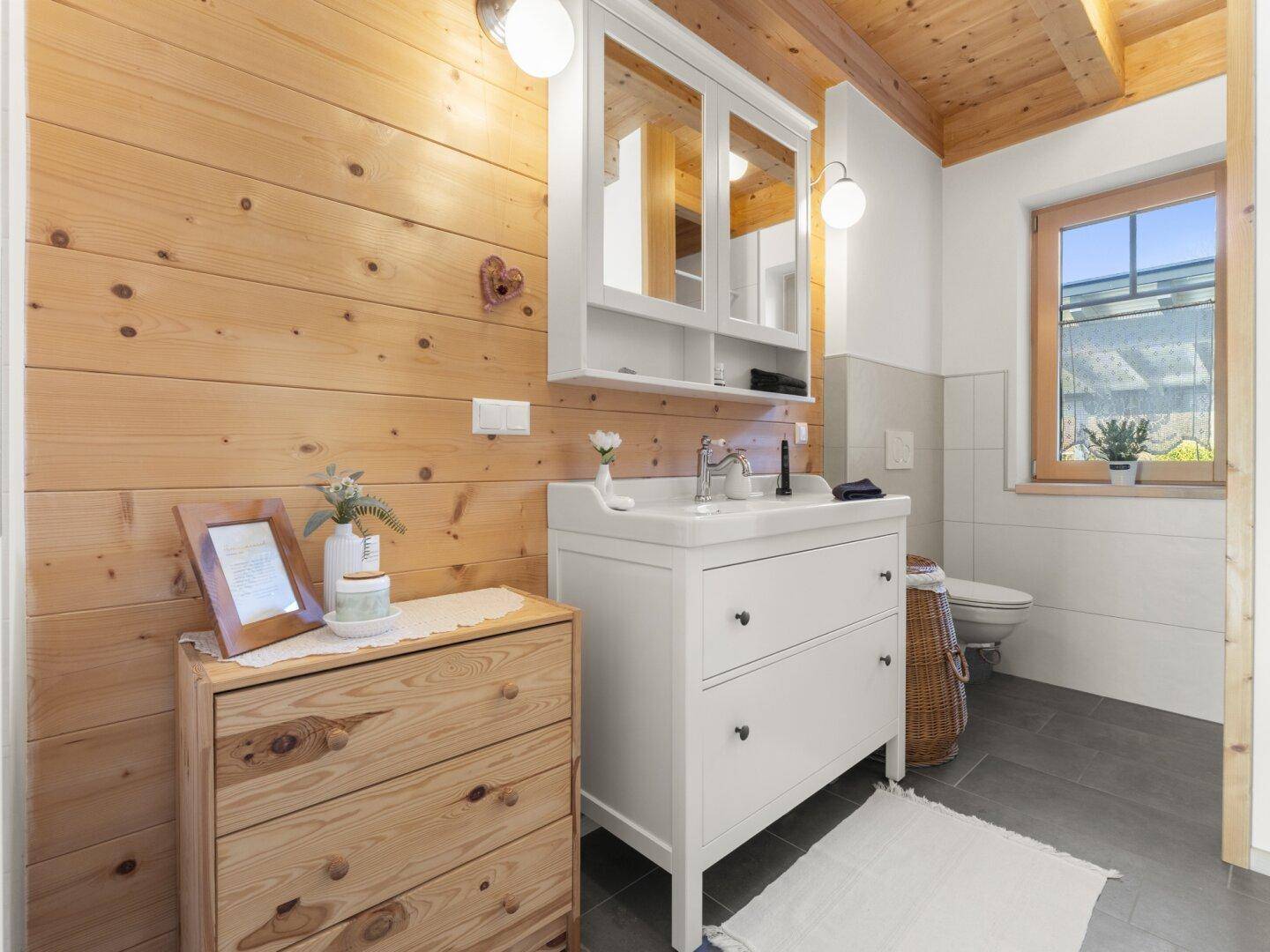 Rustikales Badezimmer mit Holzwand, Waschtisch und Spiegelschrank unter Holzbalkendecke.