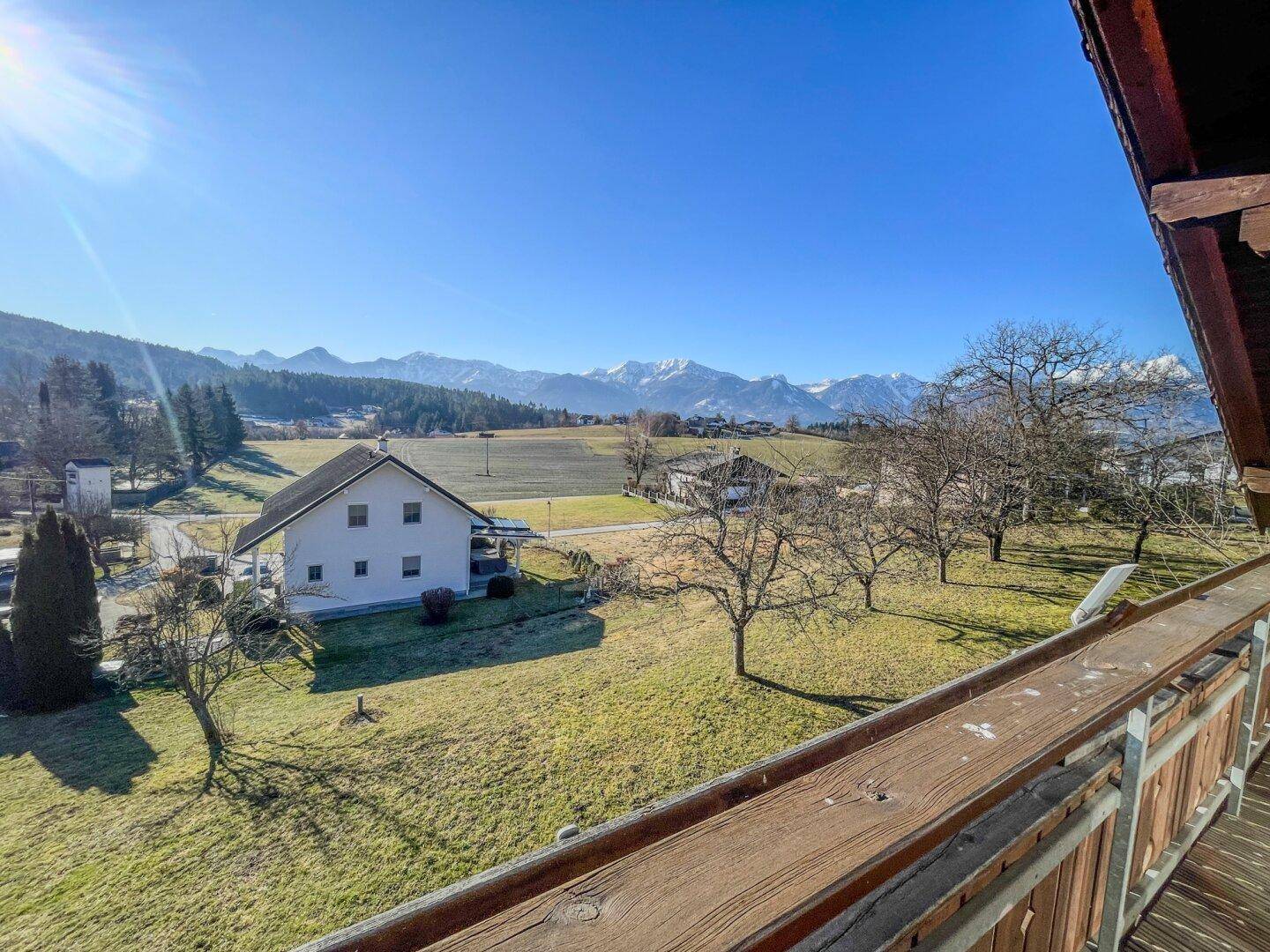 Balkon mit Holzboden und Geländer, der einen weiten Blick auf die Berge und die grüne Landschaft bietet.