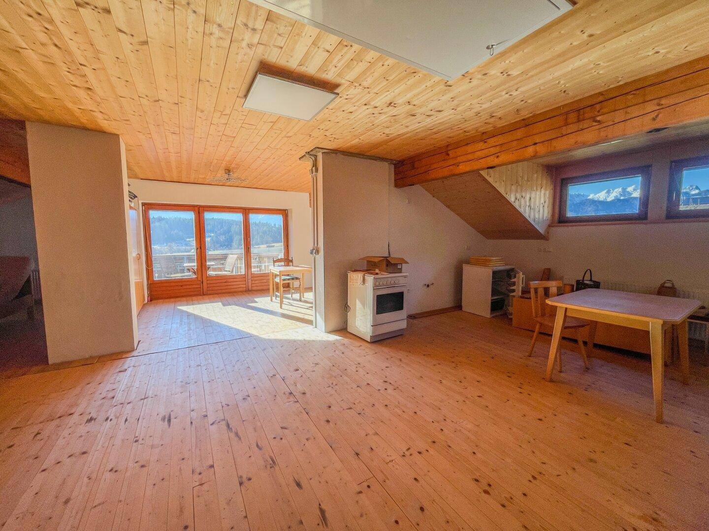 Großer, offener Raum mit Holzboden und Holzdecke, viel Tageslicht und einfacher Einrichtung.