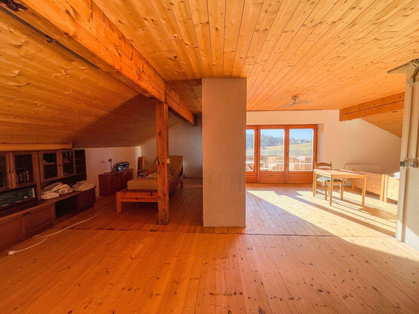 Geräumiger Bereich mit Holzboden, sichtbaren Holzbalken und Zugang zu einem Außenbereich.