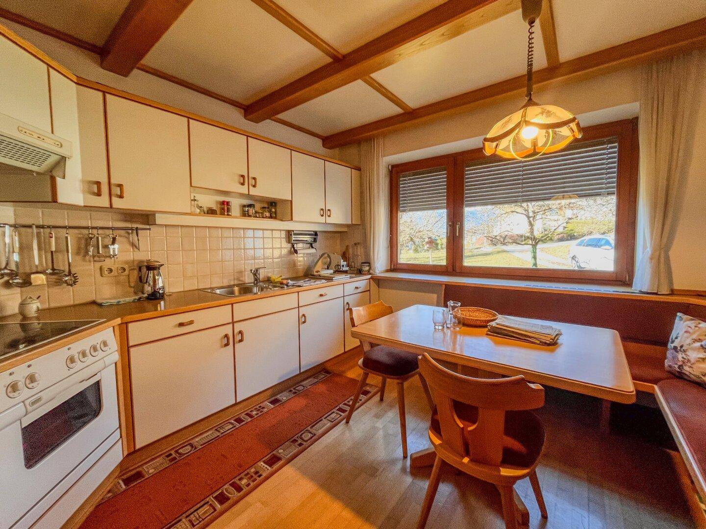 Traditionelle Einbauküche mit Essecke, Holzdecke und Fenster mit Blick ins Grüne.