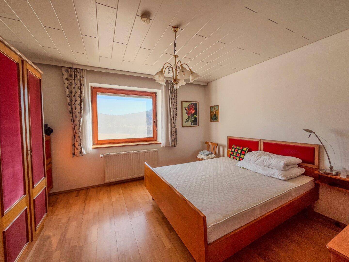 Schlafzimmer mit Holzboden, traditionellen Möbeln und einem Fenster für natürliches Licht.