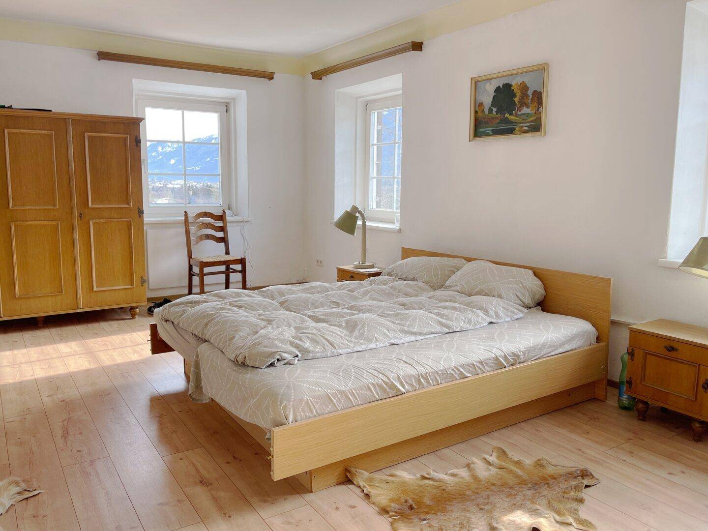 Helles Schlafzimmer mit Holzbett, Kleiderschrank und weitem Blick auf die schneebedeckten Berge.