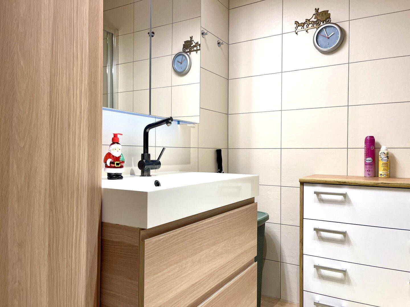 Modernes Badezimmer mit hellem Fliesenboden, Einzelwaschbecken und Holzunterschrank.