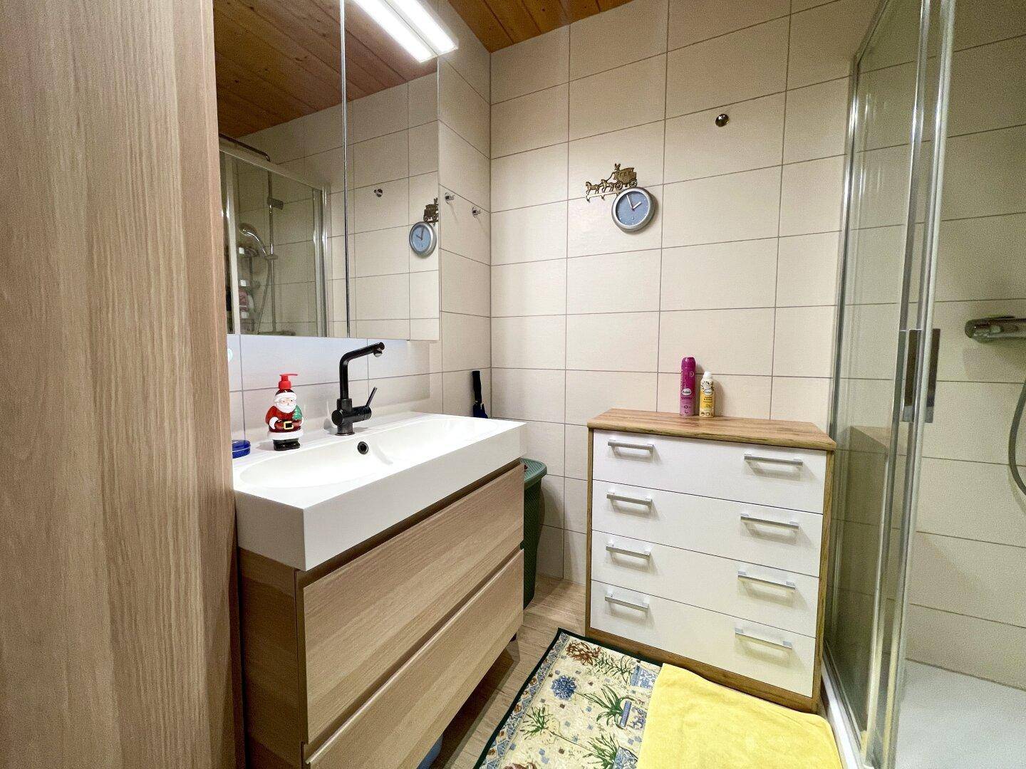 Helles Badezimmer mit Duschkabine, Einzelwaschbecken und Holzdecke, gut beleuchtet.