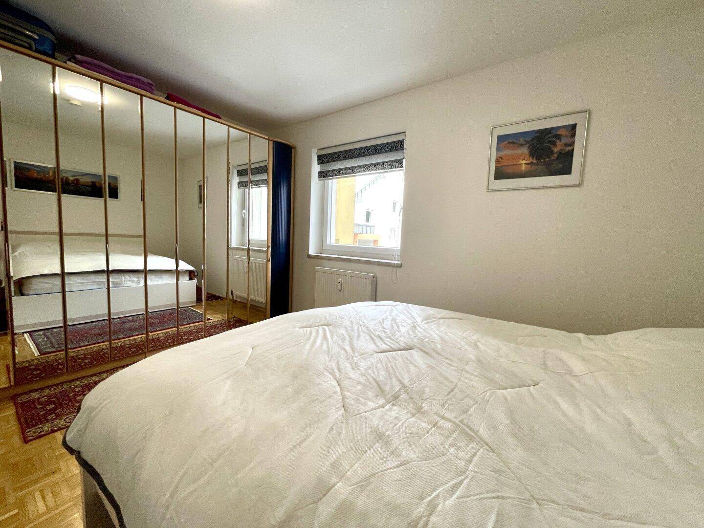 Schlafzimmer mit großem Bett, Spiegelschrank und Fenster mit Blick nach draußen.