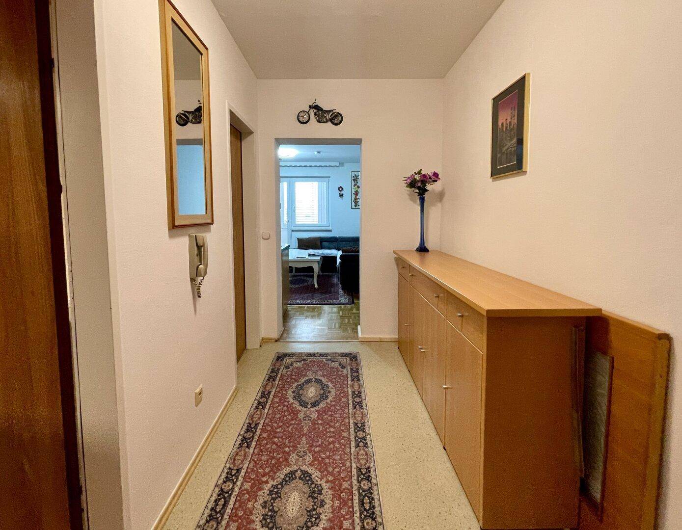 Langer, heller Flur mit Holzboden, Garderobe und Blick in den Wohnbereich.