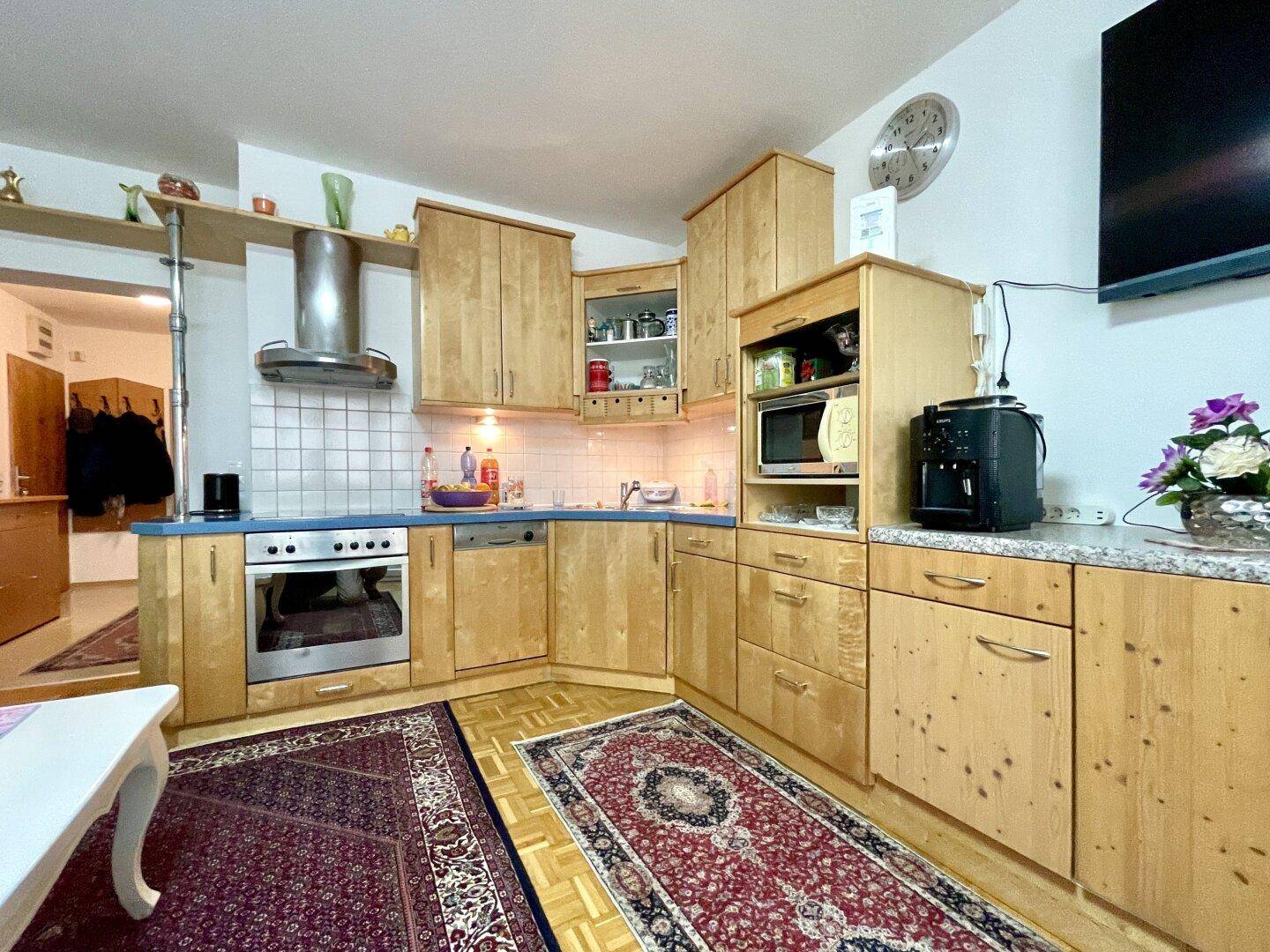 Funktionale Holzküche mit Einbaugeräten, Granitarbeitsplatte und Fliesenrückwand, offen zum Wohnbereich.