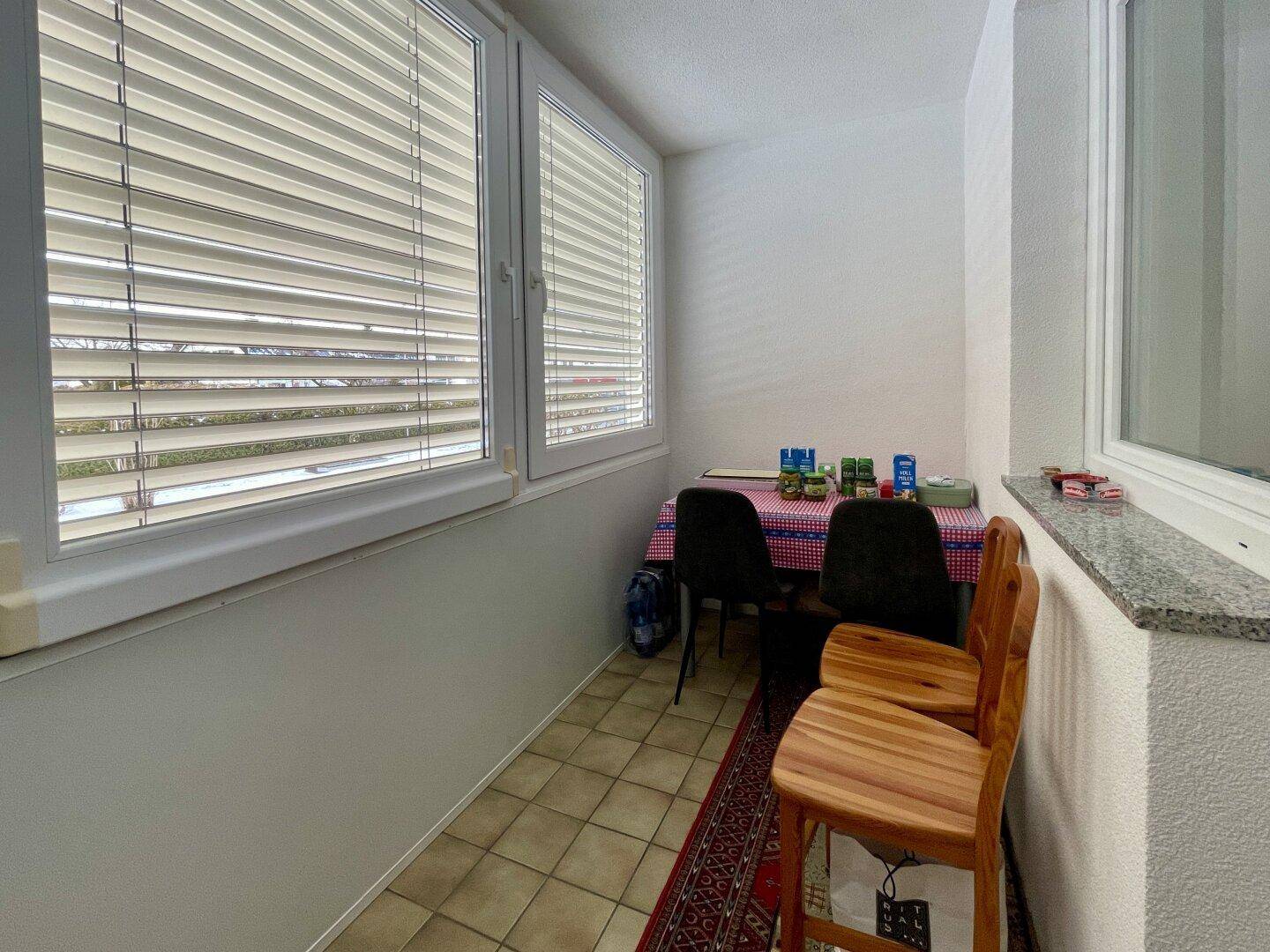 Verglaster Balkon mit Fliesenboden und kleinem Esstisch, ideal für Mahlzeiten im Freien.