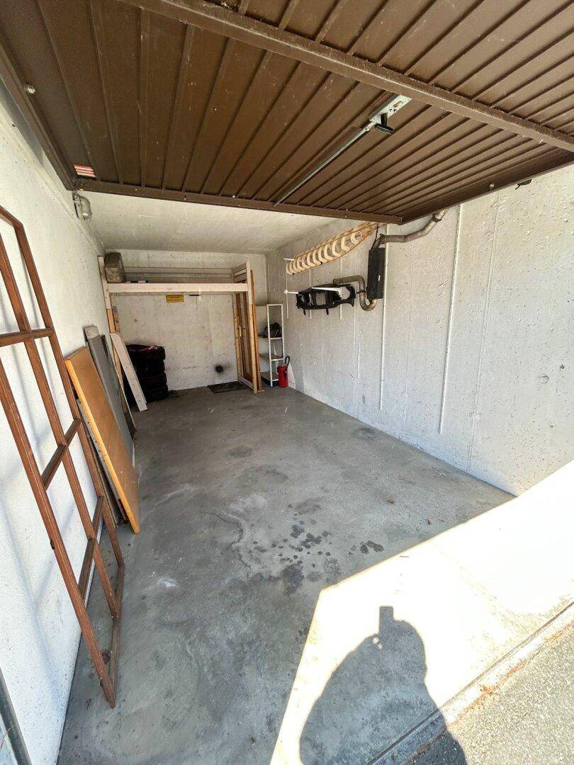 Geräumige Garage mit Betonboden, Stauraum und einem Rolltor.