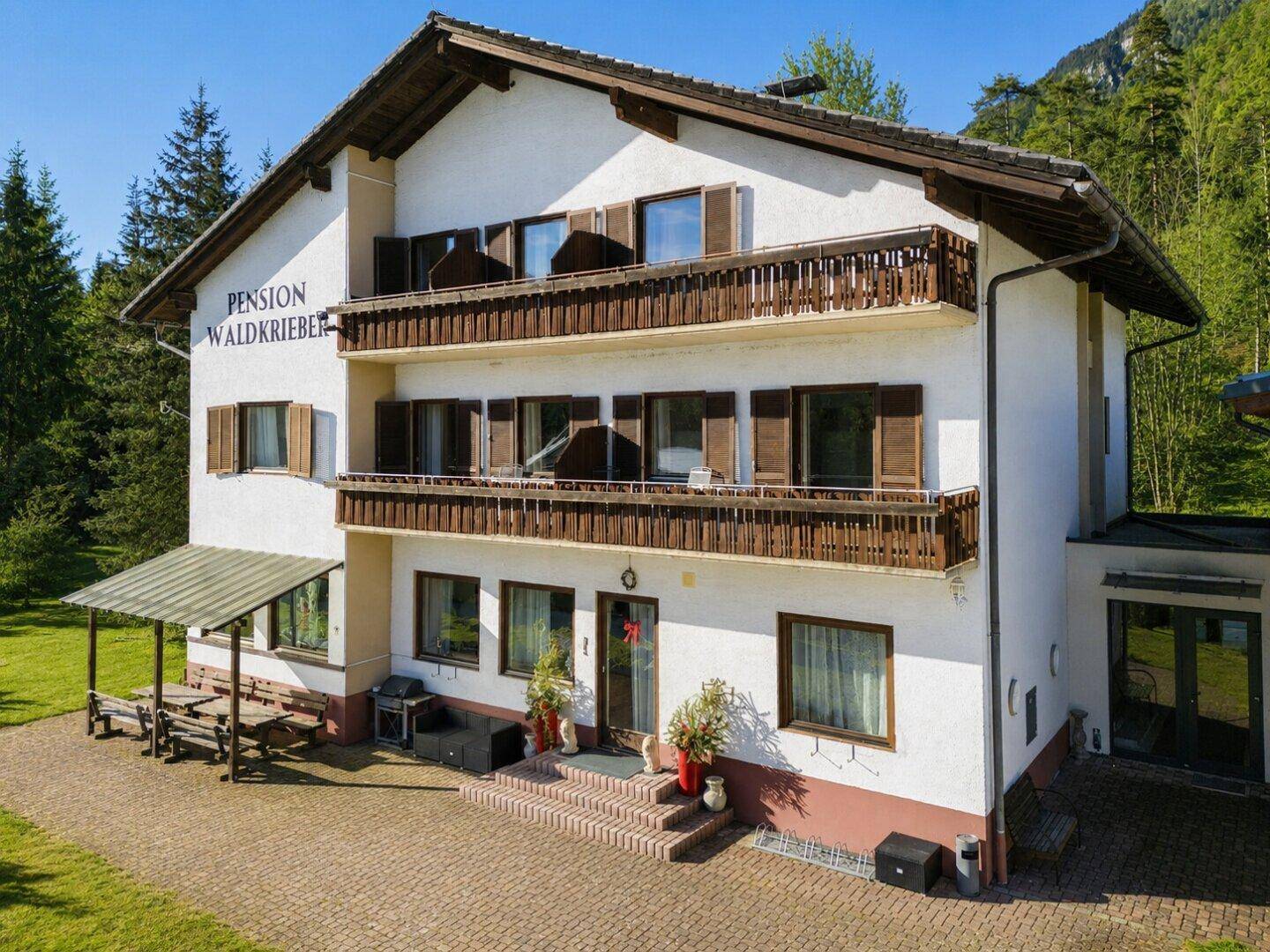 Traditionelles Pensionsgebäude mit mehreren Balkonen und umliegender grüner Landschaft.