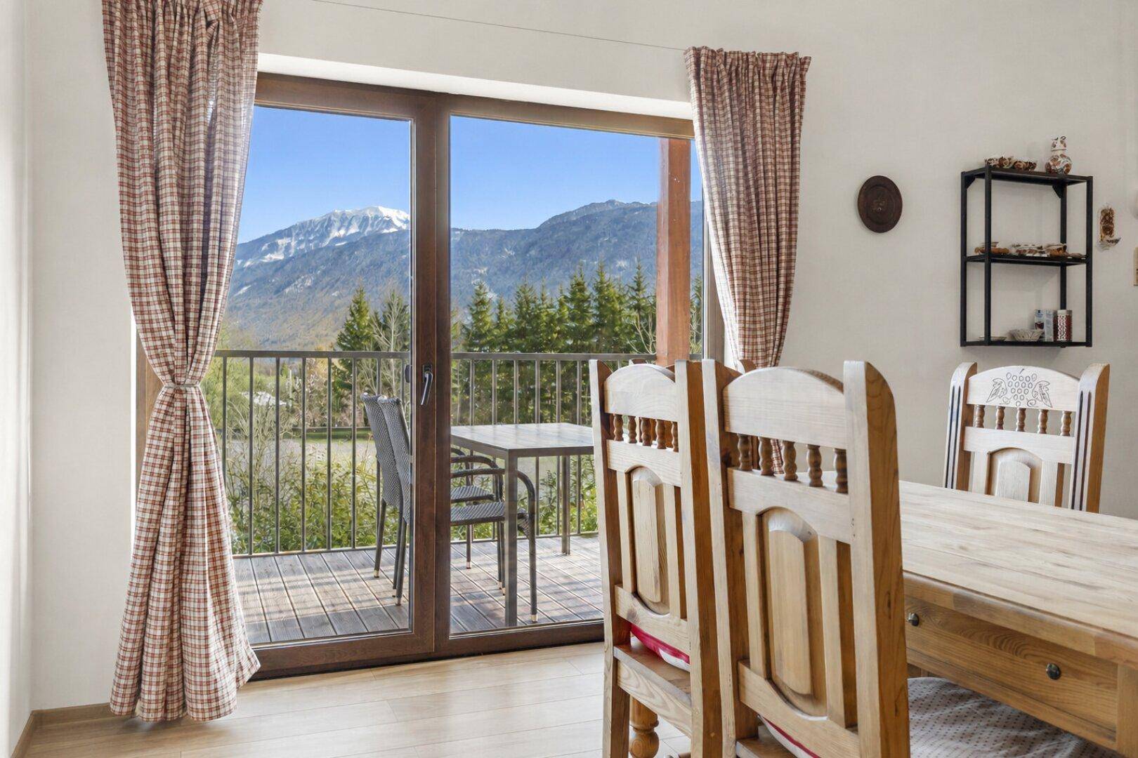 Essbereich mit Holztisch und Stühlen, direkter Zugang zu einem Balkon mit Bergblick.
