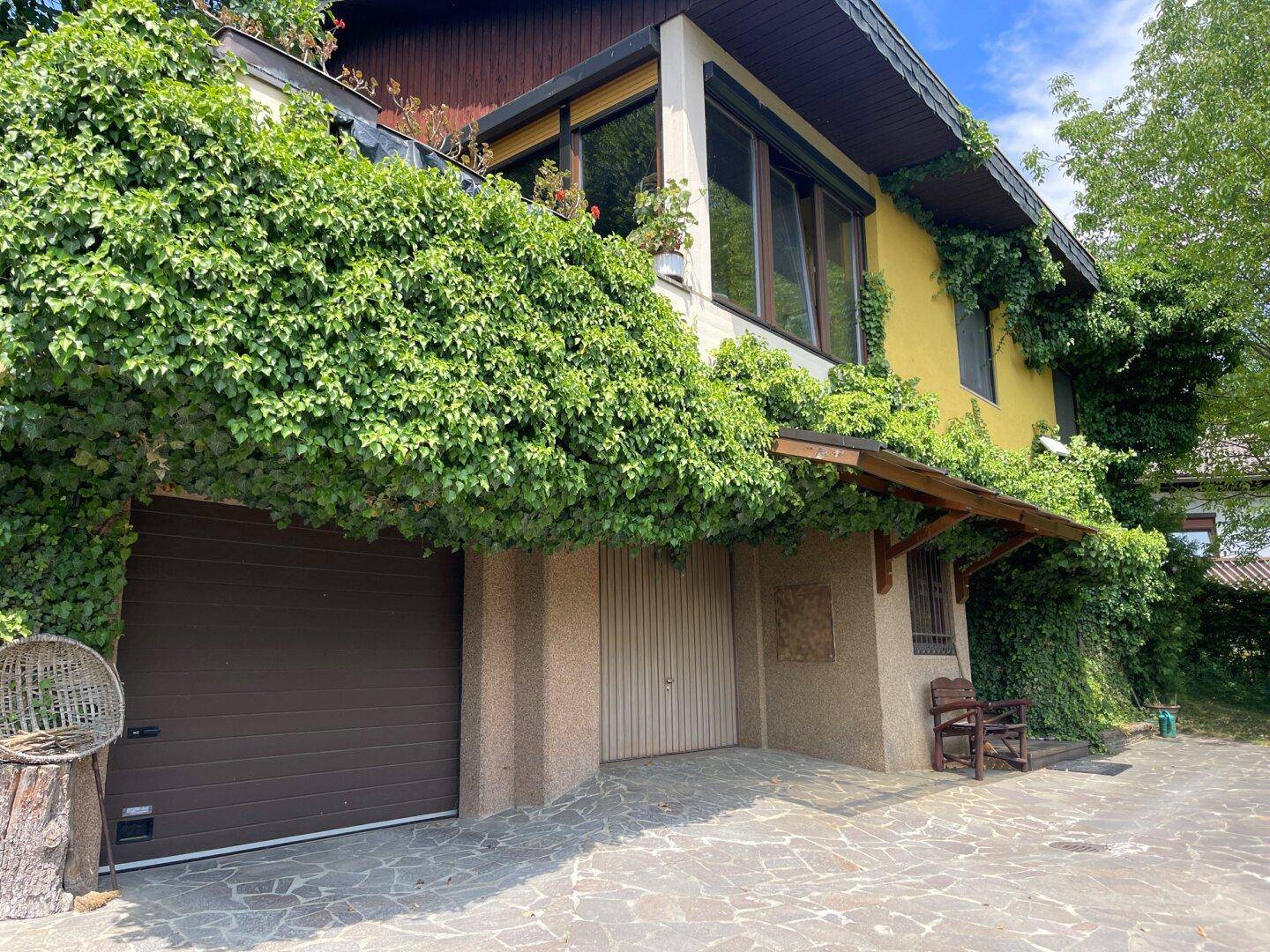 Eingangsbereich des Hauses mit Garage, umrankt von dichtem Efeu und einer gepflasterten Fläche.