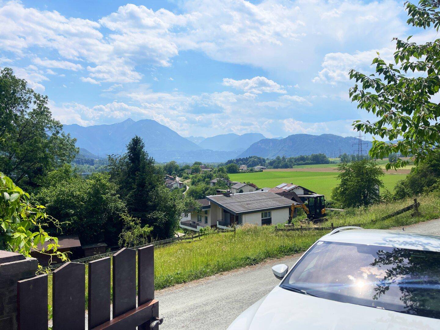 Malerischer Blick auf grüne Felder und ferne Berge unter einem blauen Himmel mit Wolken.