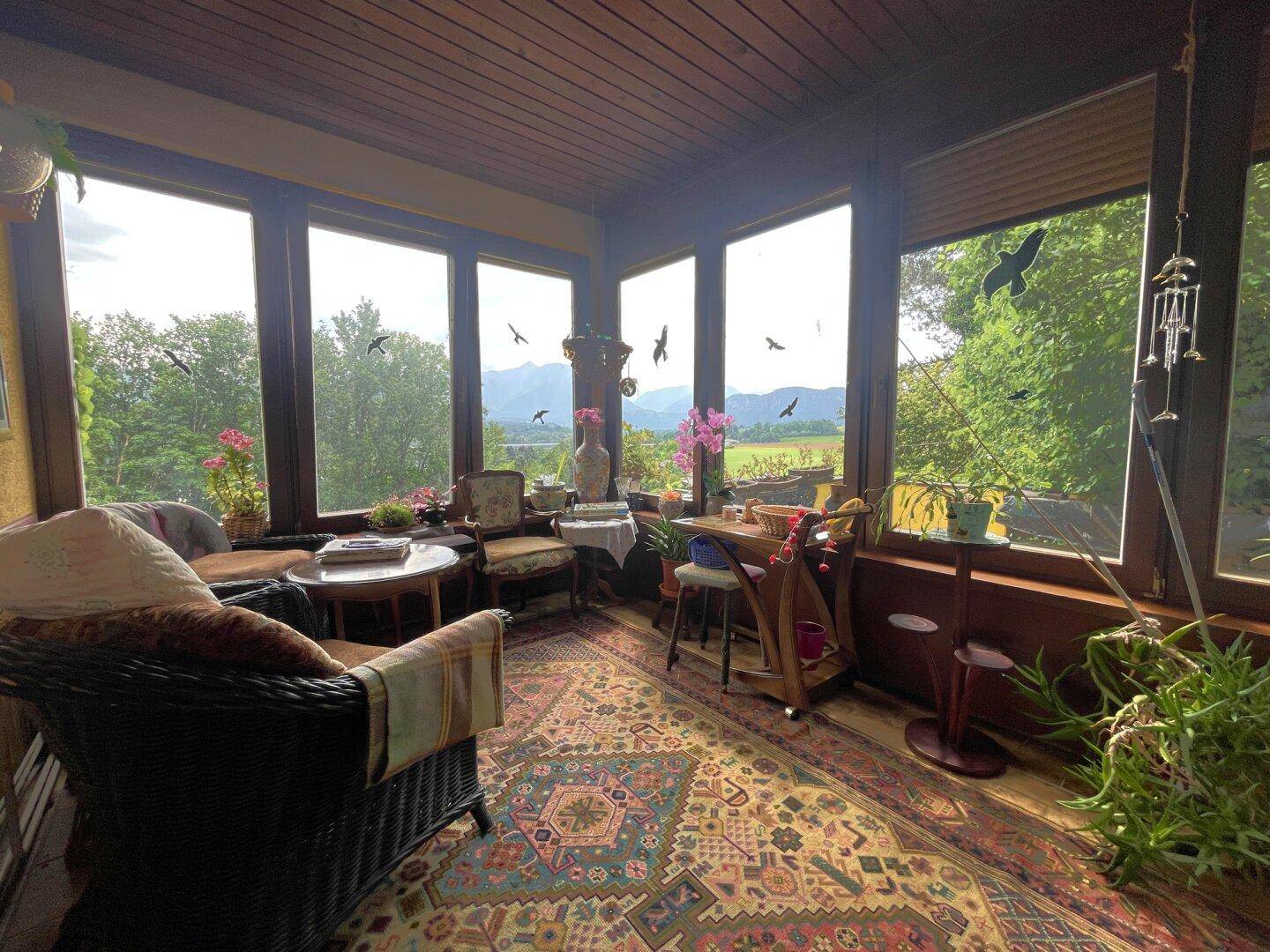 Gemütlicher Wintergarten mit großen Fenstern, Teppichboden und weitem Blick auf die Landschaft.