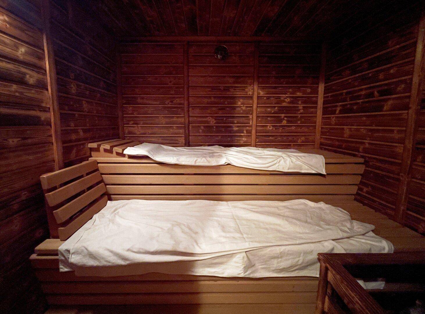 Holzvertäfelte Sauna mit zwei Liegeebenen und weißen Tüchern für Entspannung.